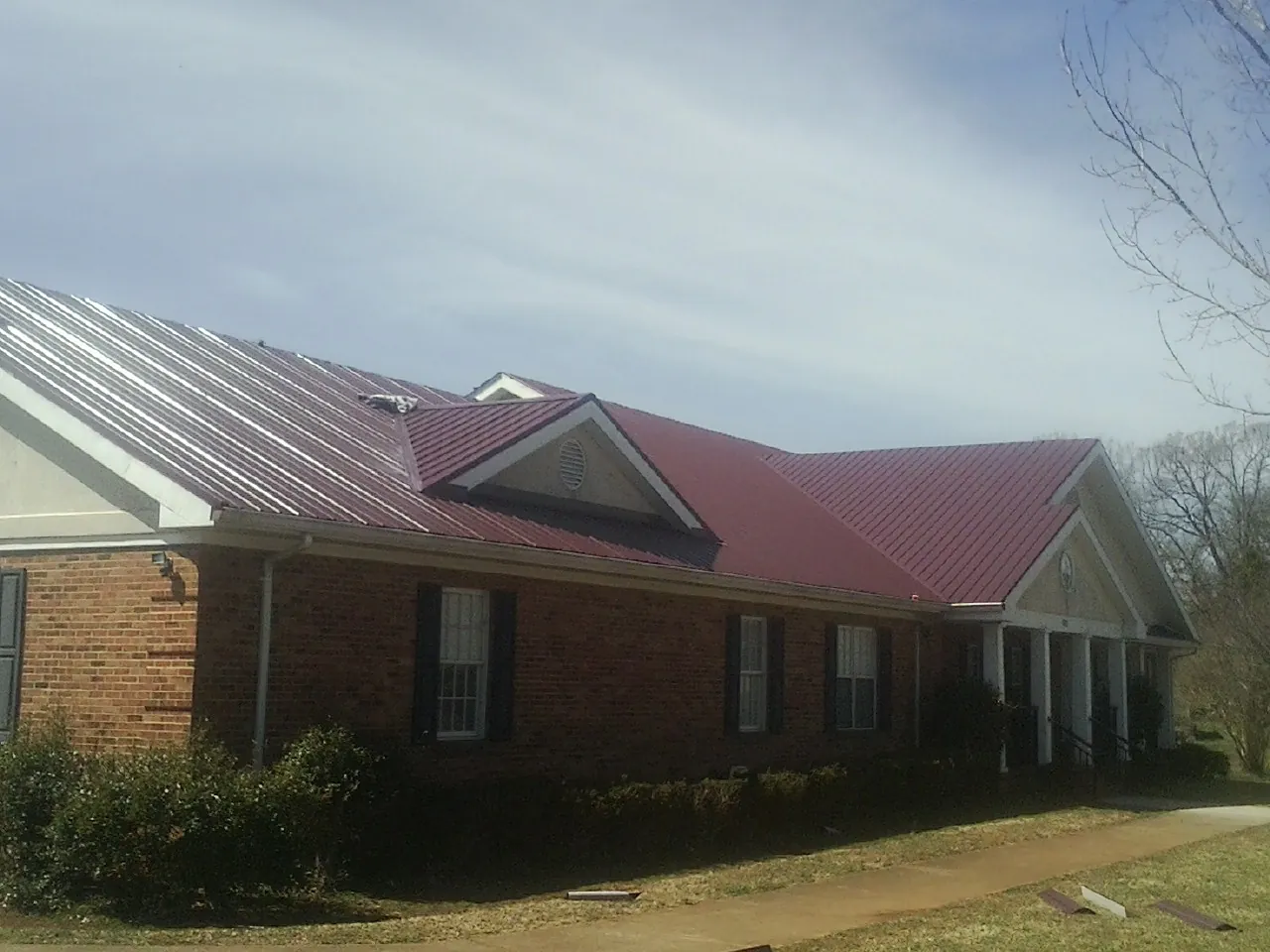 Red metal roof with gabled entries on a long brick building, from a Hail Damage Roof Repair job in Ruby