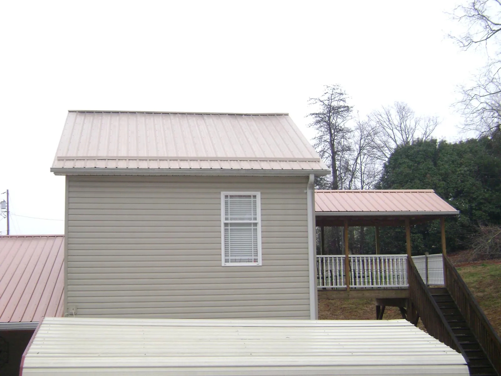 Tan metal roofs on a two story addition and attached porch, from a Roof Replacement job in Ruby